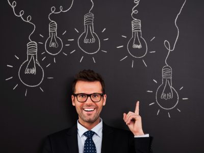 Happy man in glasses pointing at light bulbs on a chalkboard, showing creative investing ideas.