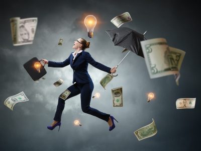 Entrepreneur in a suit walking under a storm of money and light bulbs, representing ideas.